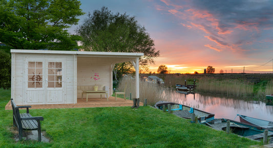 White shed with a covered area by a body of water during sunset.